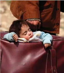  ??  ?? A child sleeps while being carried in a bag in the village of Beit Sawa, Eastern Ghouta, as 12,000 civilians fled along the ‘humanitari­an corridor’ yesterday. Photo: Omar Sanadiki