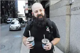  ?? Charles Rex Arbogast ?? The Associated Press Adam Taylor, a sound engineer from Las Vegas, carries two glasses of iced coffee Monday on a street in Chicago.