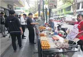  ?? SOMCHAI POOMLARD ?? A customer buys food from a street vendor in Bangkok.