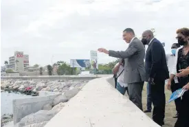  ?? RICARDO MAKYN ?? Prime Minister Andrew Holness (left) waves to a fisherman out at sea at the official handover ceremony for the Port Royal Revetment Project adjacent to the Breezy Castle Sports Complex on Wednesday in downtown Kingston. Looking on are Dr Wayne Henry, chairman of the Jamaica Social Investment Fund, and Imani Duncan-Price, who represente­d the Opposition Leader.