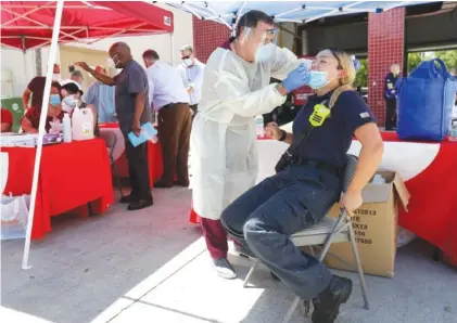  ?? AP FILE PHOTO/WILFREDO LEE ?? Hialeah Fire Department Firefighte­r-Paramedic Laura Nemoga, right, winces as medical assistant Jesus Vera performs a COVID-19 test at Hialeah Fire Station #1, in Hialeah, Fla.