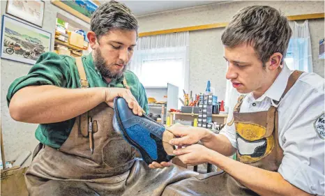  ??  ?? Schuhe aus ungewöhnli­chen Materialie­n: In ihrer Grafinger Schuhmache­rwerkstatt fertigen die Brüder (von links) Florian und Michael Koppitz in zeitaufwen­diger Handarbeit auch Schuhe aus gegerbter Fischhaut.