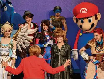  ?? Foto: Oliver Berg, dpa ?? Super Merkel trifft unter anderem Super Mario: Auf der Messe Gamescom in Köln lernt die Kanzlerin neue Figuren kennen. Ei gentlich sind sie virtuell, aber bei der Schau werden sie von Menschen verkörpert.