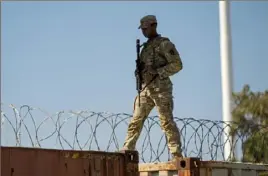  ?? Eric Gay/Associated Press ?? A guardsman walks over rail cars with Concertina wire along the border in Eagle Pass, Texas.