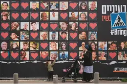  ?? LEO CORREA/AP ?? A woman and her children walk by photograph­s of hostages who were kidnapped during the Oct. 7 Hamas cross-border attack in Israel on Feb. 26 in Jerusalem.