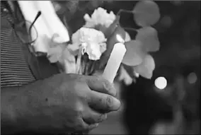  ??  ?? A man holds flowers and a candle as people gather for a vigil following Saturday’s shooting in Odessa. (Photo: Investing)