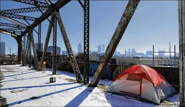  ?? DAVID GOLDMAN / AP ?? A tent sits in the snow on a bridge frequented by the homeless as Atlanta’s downtown skyline stands in the background on Thursday. The deep freeze that shut down much of the South has begun to relent.
