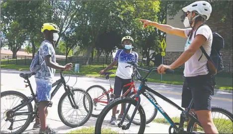  ?? (The Gazette/Liz Martin) ?? Junior Tsimba, 13, (left) and Bernoli Luvandu, 11, discuss where to ride with Audrey Wiedemeier, executive director of the Iowa City Bike Library, during Bike Club, a bike education program offered by the bike library in Iowa City, Iowa.