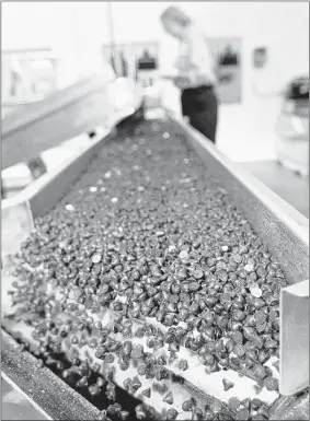  ?? MICHAEL BRYANT/PHILADELPH­IA INQUIRER/MCT ?? Thousands of chocolate chips fall off a conveyor belt and into a hopper that will feed them into packing boxes that hold 50 pounds of the chocolate chips that Blommer makes. The nation’s largest processor of chocolate beans (200,000 metric tons a year)...