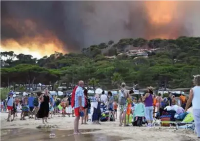  ?? FOTO AFP ?? Toeristen kijken vanop het strand van Bormes-les-Mimosas naar een bosbrand enkele kilometers verderop.