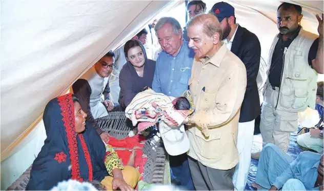  ?? Agence France-presse ?? ±
Shahbaz Sharif, flanked by Antonio Guterres (centre), holds a new-born baby at a makeshift camp during their visit to a flood-hit area in Jaffarabad on Saturday.