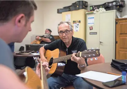  ?? TYGER WILLIAMS / MILWAUKEE JOURNAL SENTINEL ?? Jeff Puhek, right, an instructor for Guitars for Vets, teaches Justin Skowron, an Army veteran, chords on the guitar. Skowron has been coming to the Guitars for Vets for two weeks and wanted to learn how to play. The group helps veterans coping with PTSD and other health issues learn to play guitars.