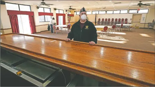  ?? (AP/Charles Krupa) ?? With chairs stacked against the wall of their hall space, Craig DeOld, commander at Veterans of Foreign War Post 1018, poses at the empty bar rail at the post’s rental space in Boston. Local bars and halls run by the VFW and American Legion posts have fallen on hard times during the coronaviru­s pandemic. Organizers say many risk permanent closing after states ordered them, like other bars and halls, to shutter last spring.