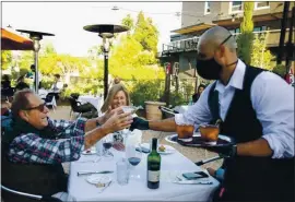  ?? FILE PHOTO BY ANNE WERNIKOFF FOR CALMATTERS ?? Doug Mahon reaches for a cocktail from a masked server at Cole’s Chop House in Downtown Napa on March 22. The popular steakhouse reopened immediatel­y following the announceme­nt that Napa restaurant­s could begin dine-in service.