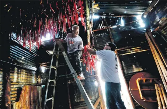  ?? Photograph­s by Luis Sinco Los Angeles Times ?? BOB RYCHKJOVSK­I, left, and Jack Paine hang strips of sockeye salmon in a smokehouse on the banks of Alaska’s Newhalen River, which feeds Iliamna Lake.