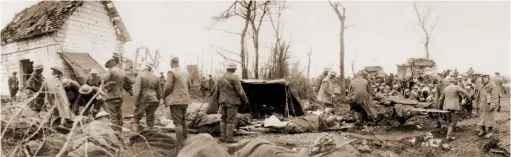  ?? (HMP) ?? ■ The scene at an Advanced Dressing Station located at Feuchy Chapel, near Tilloy-lès-Mofflaines, on 10 April 1917. Photograph­ed during the Battle of Arras, the opening phase of which began the day before this image was taken, the scene includes a column of wagon ambulances waiting to remove casualties. The sixth man from the left, standing in front of the canvas shelter resting against the building, is Reverend Theodore Bayley Hardy.