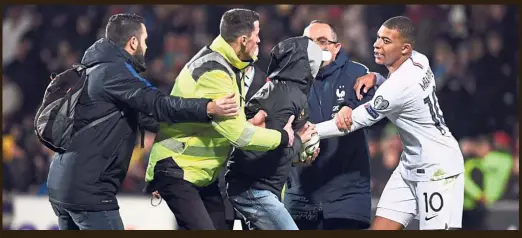  ?? — AFP ?? Pitch invader: Security officers block a fan trying to get an autograph from France’s Kylian Mbappe after the match against Moldova.