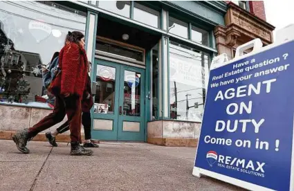  ?? Keith Srakocic / Associated Press ?? People walk by a real estate office in Pittsburgh’s Lawrencevi­lle neighborho­od. Even if it’s a stretch now, buying your first home by age 35 can mean more wealth in retirement.