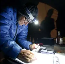  ??  ?? Race organiser Scott Worthingto­n checks the competitor list on the race’s first night. At right is the Revenant whisky bottle, which runners tap to signify they’ve pulled out, and only finishers get to taste.