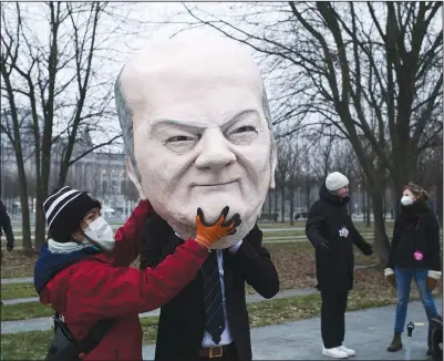  ?? (AP/Markus Schreiber) ?? One activist helps another to put on a mask of Scholz.