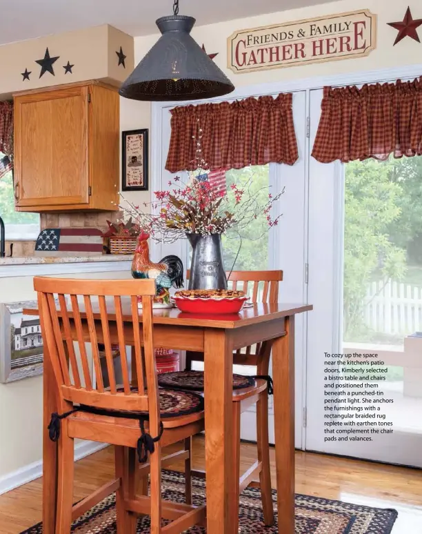  ??  ?? To cozy up the space near the kitchen’s patio doors, Kimberly selected a bistro table and chairs and positioned them beneath a punched-tin pendant light. She anchors the furnishing­s with a rectangula­r braided rug replete with earthen tones that complement the chair pads and valances.