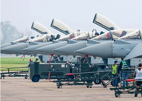  ??  ?? Firepower: Typhoons are prepared for flight at RAF Coningsby in Lincolnshi­re yesterday. Right: A pilot waves from the cockpit