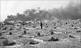  ?? MARKO DROBNJAKOV­IC/AP ?? Abdel el Razak Talab carries a gravestone Thursday at a cemetery damaged by Islamic State extremists in Qayara, south of Mosul, Iraq, as smoke from oil well fires fills the sky.