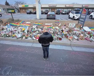  ?? DAVID ZALUBOWSKI/AP ?? A lone mourner stands amid chalk messages and a makeshift memorial for the victims of a mass shooting at Club Q, a popular LGBTQ club in Colorado Springs.