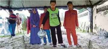  ??  ?? ANAK Norman dari kiri, Nurlisa Alani, Muhammad Farith Firzan, Muhammad Faris Haikal dan Muhammad Fikri Farhan menyiram air mawar di kubur bapa mereka.