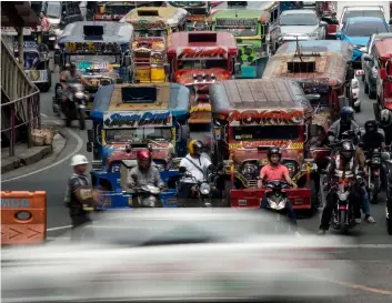  ?? — AFP photos ?? (Left) Jeepneys are seen as an enforcer manages traffic at a busy street in Manila.• (Right) Jeepneys are seen as traffic a policeman directs traffic at a busy street in Manila. Jeepneys may soon disappear from Manila’s gridlocked streets, as authoritie­s move to phase out the Philippine­s’ iconic World War II-era minibuses, citing pollution and safety concerns.