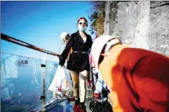  ?? AFP ?? A tourist carrying a bag of food walks along a skywalk as a group of cleaners work at Tianmen Mountain.