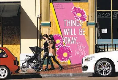  ?? NELVIN C. CEPEDA U-T ?? Two women, one pushing a baby stroller, walk past a mural on Market Street between Fifth and Sixth avenues on Friday in downtown San Diego. A nighttime curfew goes into effect at 10 p.m. today.