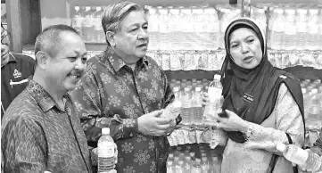 ??  ?? Siti Salmiah (right) and Kamarudin (centre) with a bottle of mineral water sold by the SMK Tansau cooperativ­e.