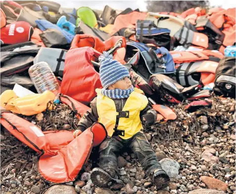  ??  ?? Amid the discarded equipment of a perilous journey, a child waits for help on a beach on the Greek island of Lesbos yesterday after crossing the Aegean sea from Turkey