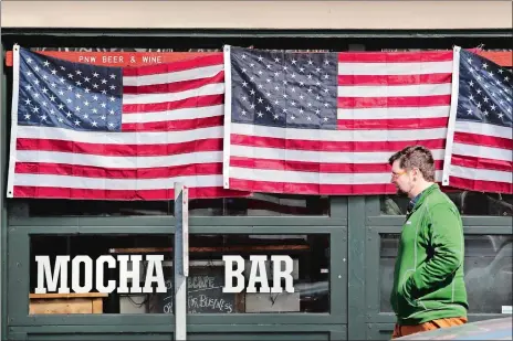  ?? ELAINE THOMPSON/AP PHOTO ?? A pedestrian walks past a closed cafe with its windows covered in American flags at the Pike Place Market on Friday in Seattle. Restaurant­s, except for take-out orders, are closed, workers who can are working from home and people are being asked to maintain physical distance from others to help stop the spread of COVID-19. Washington state health officials reported eight new coronaviru­s-related deaths on Friday, bringing the total to 83. Seven of those deaths were in King County, the epicenter of the outbreak in the state.