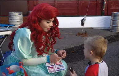  ?? Ryan Mancini/The Signal ?? Camden Alexie, 2, gets ready for a temporary tattoo from Dawn Smith, owner of Pacific Princess Parties. She dressed up as Ariel from “The Little Mermaid” while at the Holiday Extravagan­za Boutique at Wolf Creek Brewery.