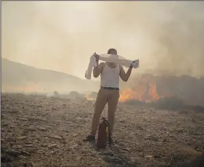  ?? (File Photo/ap/petros Giannakour­is) ?? A man wraps his shirt over his face July 24 as he tries to extinguish a fire near the seaside resort of Lindos, on the Aegean Sea island of Rhodes, southeaste­rn Greece.