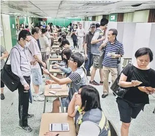  ?? — Gambar AFP ?? BUANG UNDI: Seorang sukarelawa­n menyerahka­n kad pengenalan pengundi sejurus mendaftark­annya di sebuah pusat pengundian di Hong Kong, semalam.