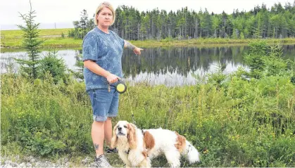  ?? SHARON MONTGOMERY-DUPE • CAPE BRETON POST ?? Jennifer Lemoine of New Waterford, with her dog Winston, points to the location where a live beaver trap was recently left on the bank of the pond along the Summit Recreation­al Trail in Scotchtown which almost killed her dog. Lemoine said the beavers were a huge part of the enjoyment of the trail but were killed off with approval by Nova Scotia Lands and Forestry due to a flooding issue rather than relocated.