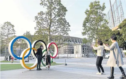  ?? THE NEW YORK TIMES ?? People take photos with the Olympic rings in Tokyo as the 2020 Games have been postponed until next year.