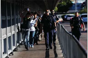  ?? AP/MARCO UGARTE ?? U.S. Customs and Border Protection agents escort Central American migrants across the Internatio­nal Bridge from Laredo, Texas, to Nuevo Laredo, Mexico, after their processing Thursday. The number of border crossings dropped in June because of hot weather and a crackdown by Mexico on migrants at its southern border.