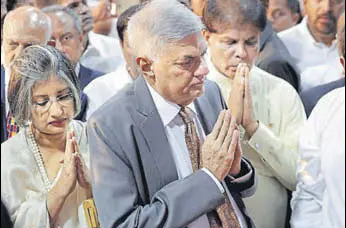  ?? AP ?? Sri Lanka's reinstated Prime Minister Ranil Wickeremes­inghe (centre) greets monks with his wife Maithree (left) after assuming duties in Colombo on Sunday.