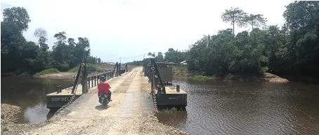  ??  ?? A motorcycli­st crosses the bridge over the crocodile-infested Bakong River. The reptiles are often seen sunbathing along the banks at the nearby Kampung Beluru.