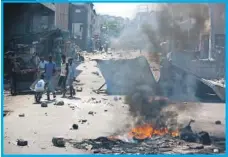  ??  ?? Personas pasan frente a la quema de controles establecid­os por los manifestan­tes en Haití