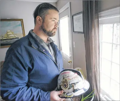  ?? MITCH MACDONALD/SALTWIRE NETWORK ?? John Holmes holds his old hardhat while looking out the window of his home in Murray Harbour, P.E.I. Holmes wants to raise awareness about mental health and career retraining supports offered in P.E.I. to former oilpatch workers struggling with the industry’s decline.