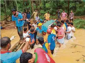  ?? (Foto STR) ?? Petugas penyelamat membantu penduduk tempatan menyeberan­gi kawasan ditakungi air susulan banjir di Kerala, India, kelmarin.