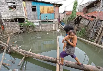  ?? Foto: Profimedia ?? Manila, Filipíny Na periférii hlavního města Filipín vrávorá matka s dítětem na kládách provizorní­ho „mostu“položeného přes ulice zatopené po řádění tajfunu.