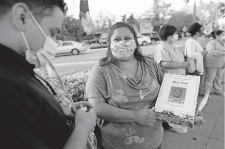  ?? [GARY CORONADO/ TRIBUNE NEWS SERVICE] ?? Danny Hernandez, left, environmen­tal services manager of Riverside Community Hospital, and Dora Reaza, right, holding a photo of her mother given to her by Lorena Jimenez, along with co-workers, family and friends hold a candleligh­t vigil for Dora's mother Rosa Luna, at Riverside Community Hospital, on May 15 in Riverside, California. Luna, an Environmen­tal Services Housekeepe­r for 25 years at Riverside Community Hospital, died from COVID-19.