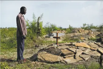  ?? Ben Curtis / Associated Press ?? South Sudanese refugee James Malish, whose mother and sister recently died days apart, stands by the grave of his mother, Joyce Doru, this month near the camp in Bidi Bidi, Uganda.