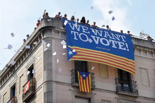  ?? PHOTO AFP ?? Un groupe de personnes a lancé des bulletins de vote du toit d’un édifice portant une bannière proréféren­dum, hier, sur la place Sant Jaume, à Barcelone. Les manifestat­ions dans la capitale administra­tive de la Catalogne s’étaient toutefois calmées,...